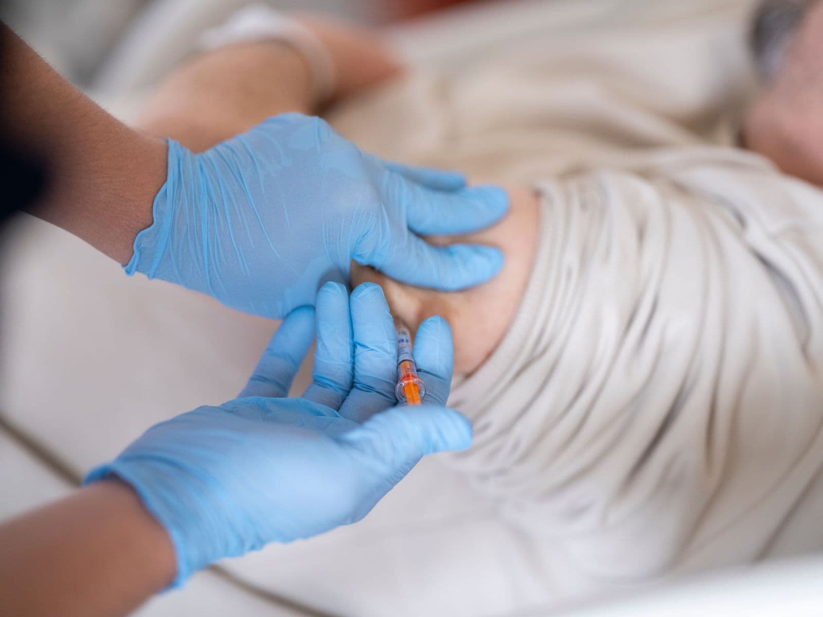Profissional de saúde com luvas azuis aplicando injeção subcutânea em um paciente