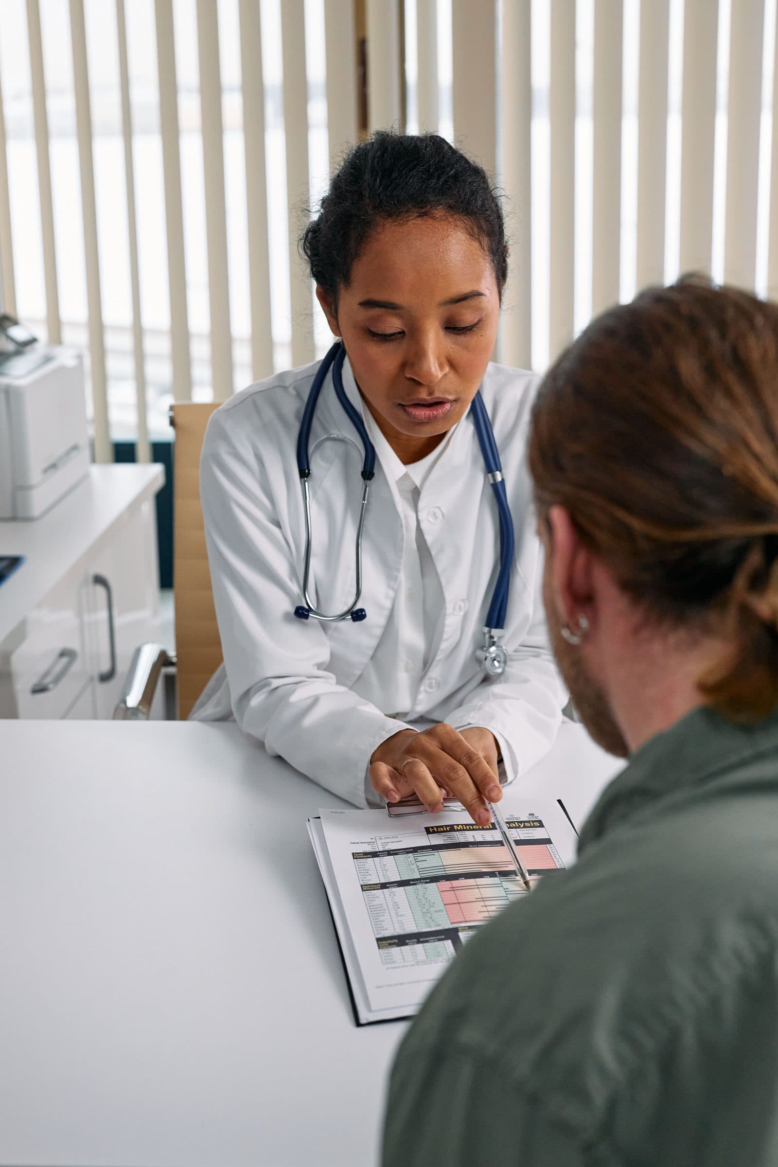 Médica apontando o laudo impresso enquanto explica o resultado ao paciente no consultório