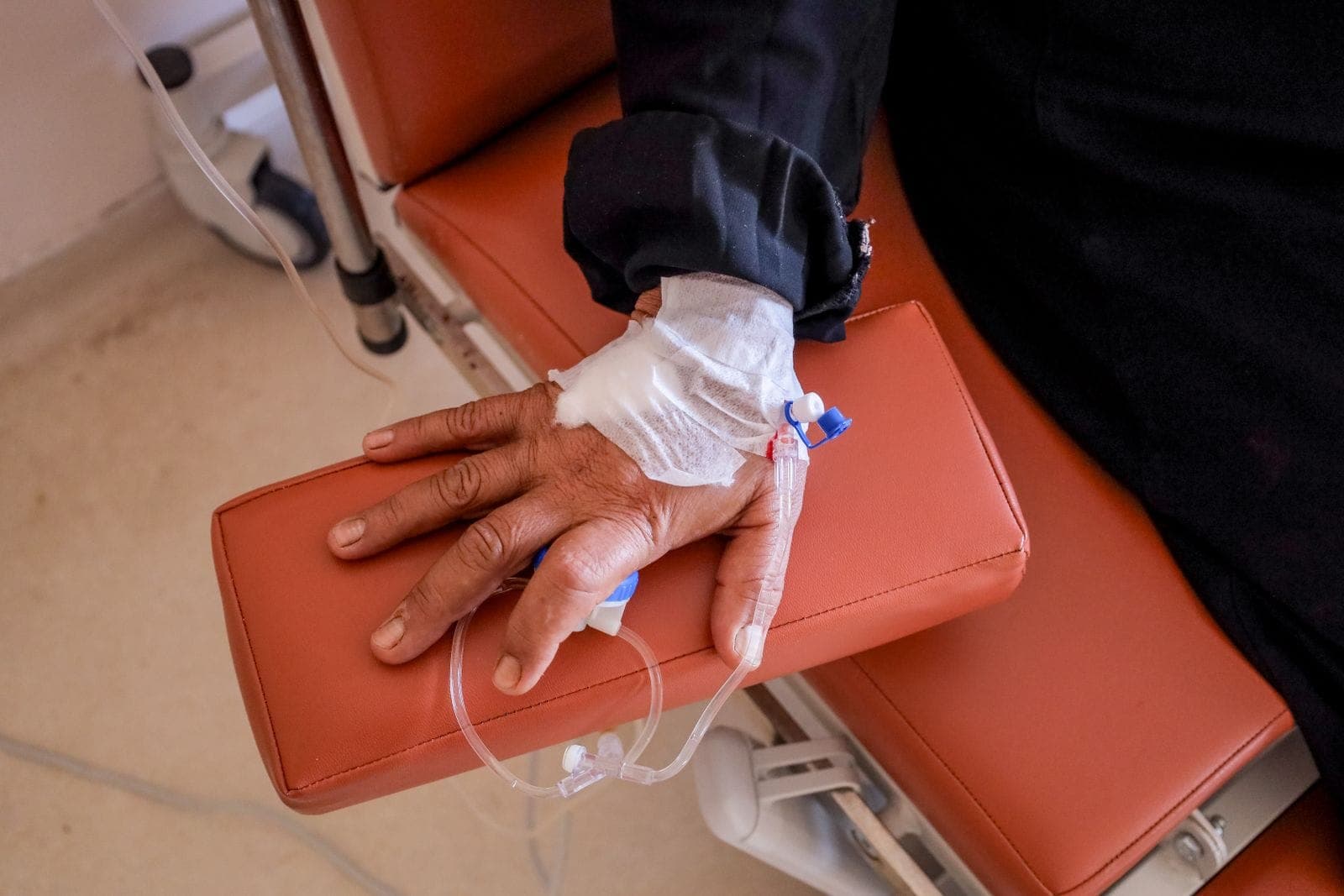 Mão de paciente com acesso venoso durante infusão em poltrona de tratamento