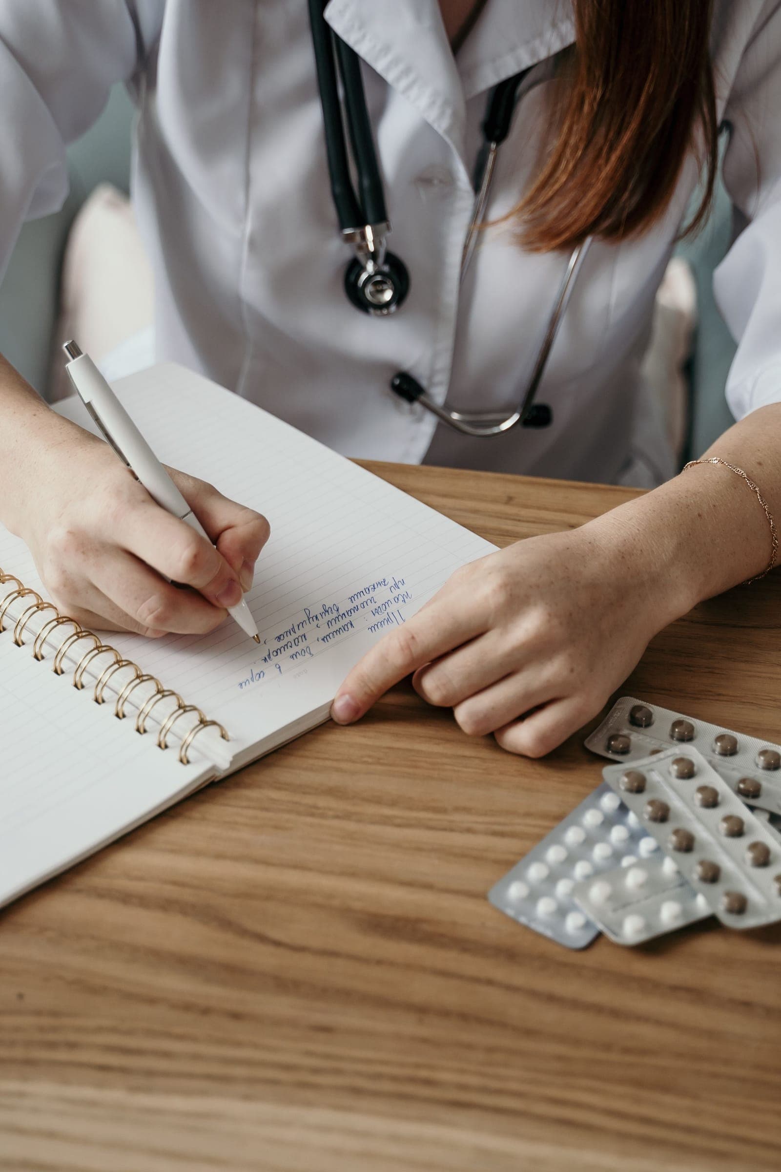 Médica escrevendo receita médica com medicamentos sobre a mesa