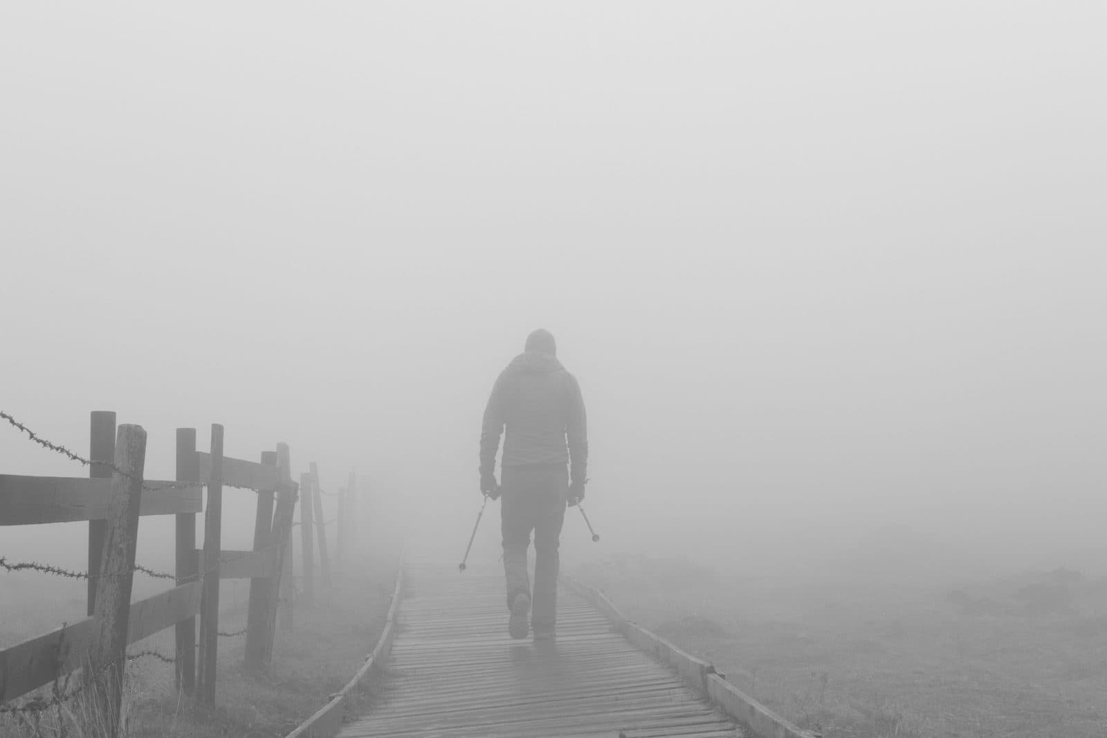 Homem caminhando sozinho por passarela de madeira em meio à neblina