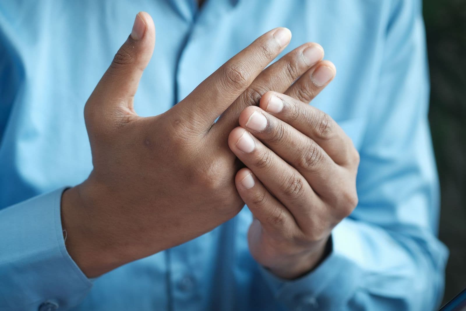 Close das mãos de um homem massageando os próprios dedos, sugerindo formigamento