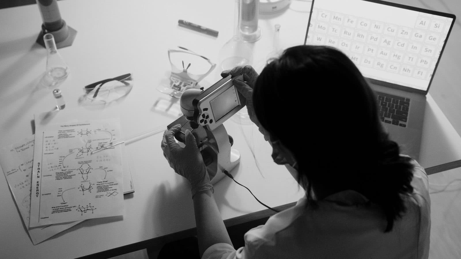 Cientista analisando amostra em microscópio digital acoplado a monitor