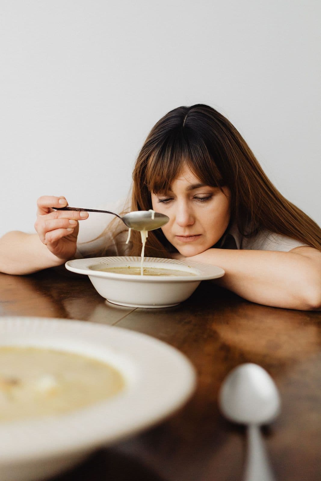 Mulher apoiada na mesa diante de um prato de sopa, sem vontade de comer